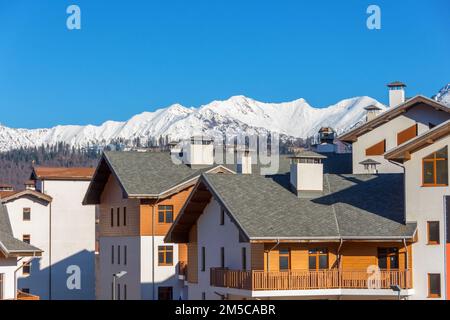 Edificio residenziale in legno con tetti spioventi in stile europeo sullo sfondo di una cima innevata di montagna con foreste e cielo blu Foto Stock