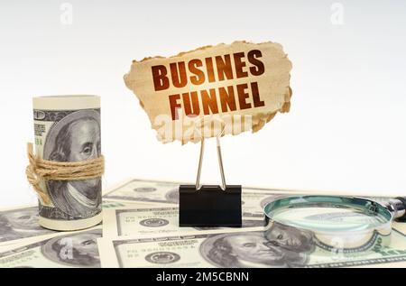 Concetto aziendale. Tra i dollari si trova una lente d'ingrandimento e vi è una clip e un segno di cartone con l'iscrizione - Business Funnel Foto Stock