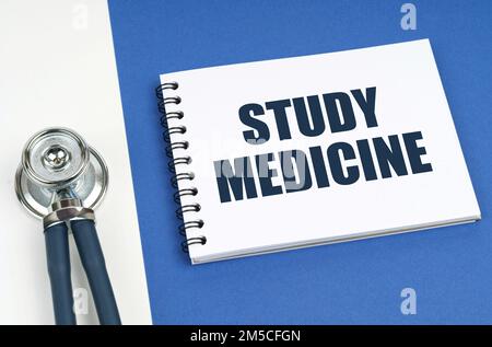 Concetto medico. Su una superficie blu-bianca si trova uno stetoscopio e un blocco note con l'iscrizione - Study Medicine Foto Stock