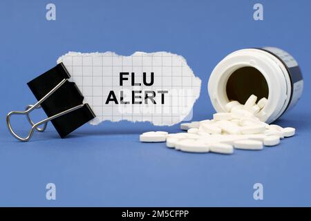 Concetto di medicina. Sulla superficie blu si trova un vasetto di pillole e una clip con carta su cui è scritto - influenza allerta Foto Stock