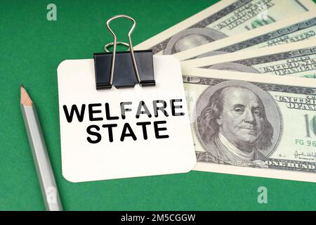 Concetto aziendale. Su una superficie verde, una penna, dollari e in una carta da clip con l'iscrizione - Welfare state Foto Stock