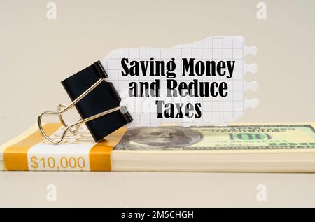 Concetto aziendale. Su una superficie grigia è un pacco di dollari su cui c'è una clip con carta strappata e l'iscrizione - risparmio di denaro e ridurre le tasse Foto Stock