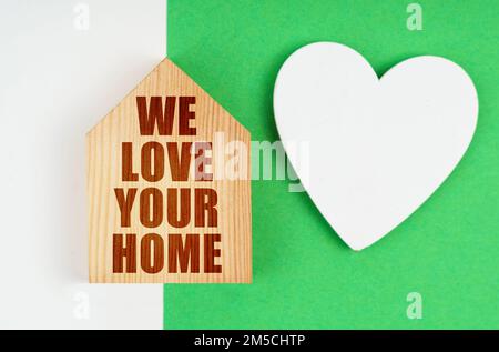 Su una superficie bianco-verde, un cuore e una casa con l'iscrizione - amiamo la vostra casa. Concetto positivo. Foto Stock