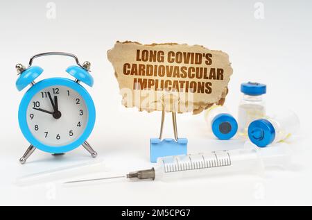 Concetto medico. Vicino allo stetoscopio ci sono una siringa, fiale e una clip con una piastra di cartone - COVID lunghi implicazioni cardiovascolari Foto Stock