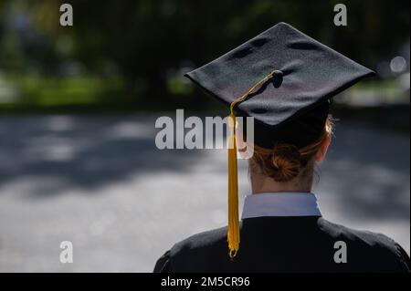 Una donna lancia il suo cappellino di laurea contro il cielo blu. Foto Stock