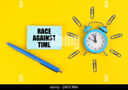 Concetto industriale. Sulla superficie gialla c'è un orologio sveglia, una penna e adesivi con l'iscrizione "Race Against Time" Foto Stock