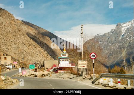 Vista panoramica invernale dalla strada asfaltata nelle montagne coperte di neve e alberi sul lato della strada su uno sfondo di cielo blu e nuvole Foto Stock