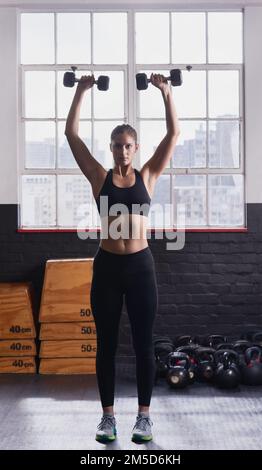 Divertiti a sudare. una giovane donna che fa esercizi di sollevamento pesi in palestra. Foto Stock