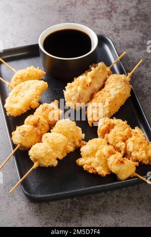 Kushikatsu in stile giapponese spiedini fritti in profondità primo piano sul piatto sul tavolo. Verticale Foto Stock