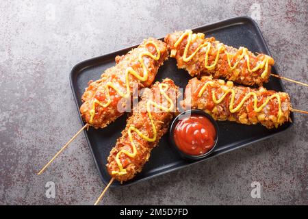 I cani corn coreani sono hot dog, formaggio, patatine fritte in una pastella su un bastone e condite con zucchero, ketchup, mostarda closeup sul piatto sul Foto Stock