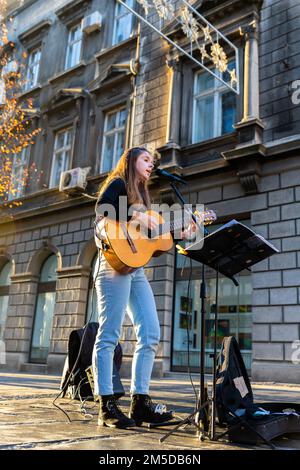 Belgrado, Serbia - 23 dicembre 2022: Musicista femminile che suona chitarra acustica e canti all'aperto nella famosa strada pedonale chiamata Knez Mihailova in Foto Stock