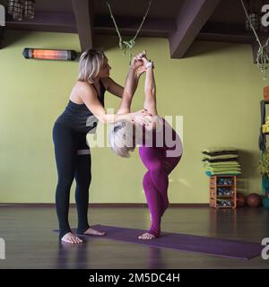 Una trainer donna conduce una lezione personale e aiuta lo studente a eseguire l'esercizio di garudasana, la posa dell'aquila, allenarsi in abbigliamento sportivo mentre si è in piedi su un Foto Stock