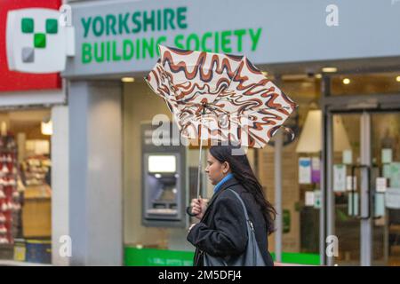 Donna che tiene un ombrello rovesciato fuori dalla Yorkshire Building Society a Preston, Lancashire. 2022 dicembre, Meteo del Regno Unito. Negozi, negozi, negozi come la pioggia pesante cade nel centro di Preston. Una banda di piogge si estende in tutto il Regno Unito, raggiungendo il nord della Scozia entro la sera. Localmente pesante e persistente, principalmente a nord e ad ovest. Foto Stock