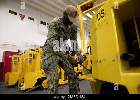 220304-N-VJ326-1064 SAN DIEGO (4 marzo 2022) – Aviation Electrician’s Mate 3rd Class Kyle Seal, di Detroit, regola una catena di ancoraggio nella baia di hangar a bordo di una nave d’assalto anfibia USS Tripoli (LHA 7), marzo 4. Tripoli è una nave d'assalto anfibio di classe americana ospita a San Diego. Foto Stock