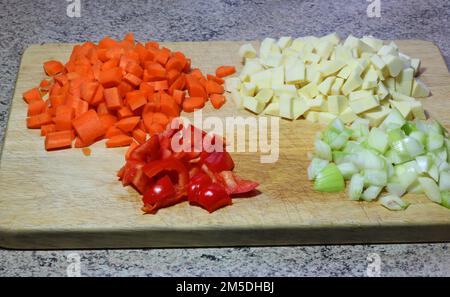 Verdure tritate su un asse di legno pronte per l'uso in un'azienda per la produzione di zuppe. Carote, cipolle, peperoni rossi e pastinaca. Foto Stock