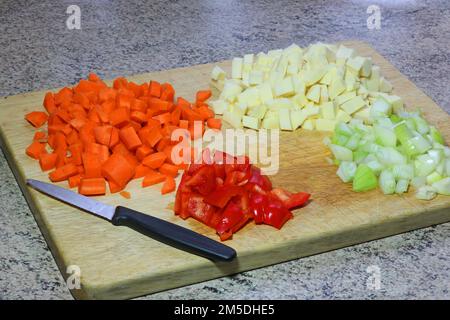 Verdure tritate su un asse di legno pronte per l'uso in un'azienda per la produzione di zuppe. Carote, cipolle, peperoni rossi e pastinaca. Foto Stock