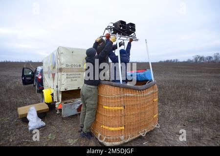 Preparativi per il mongolfiera: Gli operai di uomini impostano il bruciatore a gas sulla parte superiore del cestino, dell'automobile e del rimorchio con l'apparecchiatura su un fondo Foto Stock