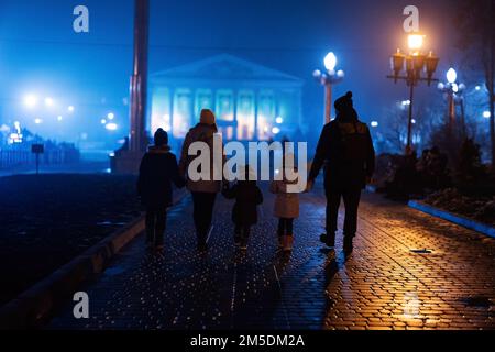 Ritorno della famiglia a piedi nella città nebbiosa di notte. Foto Stock