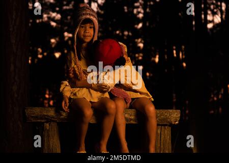 Carino piccole sorelle caldo vicino al fuoco all'aperto in tempo freddo. Bambini che si divertono al fuoco del campo. Campeggio con bambini in pineta invernale. Felice Foto Stock