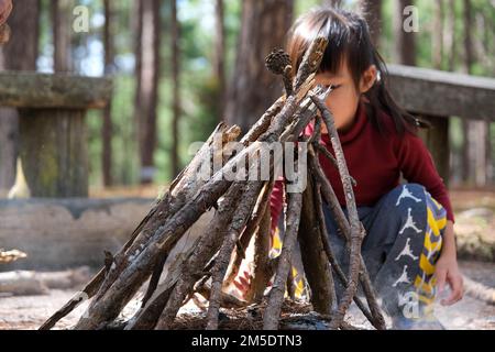 Carino piccole sorelle che fanno fuoco in boschi naturali. Bambini che si divertono al fuoco del campo. Campeggio con bambini in pineta invernale. Famiglia felice su va Foto Stock