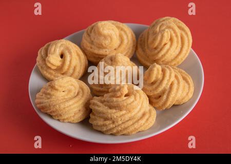 foto di diverse meringhe simili a una spirale che giace su un piatto bianco su sfondo rosso Foto Stock