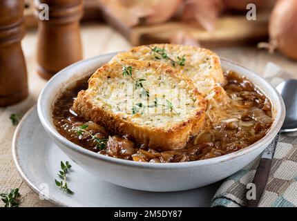 Zuppa francese di cipolle con baguette di formaggio tostato guarnita con timo su un rustico tavolo di legno Foto Stock