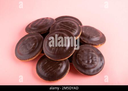 foto di un mucchio di biscotti rotondi ricoperti di cioccolato in primo piano su sfondo rosa Foto Stock