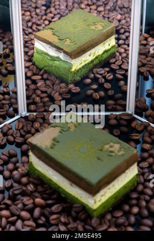 Sul foglio acrilico nero viene presentata la torta di formaggio Matcha al cioccolato fondente fatta in casa e i chicchi di caffè arrostiti con riflesso nello specchio. Selezione f Foto Stock