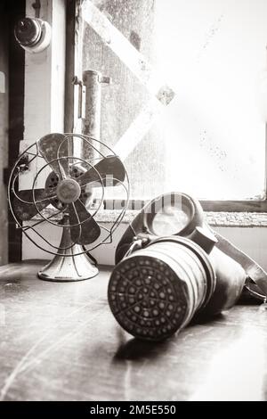 Un colpo verticale di un ventilatore elettrico d'epoca e di una maschera a gas della seconda guerra mondiale che si posano su una scrivania in tempo di guerra nella vale Foto Stock