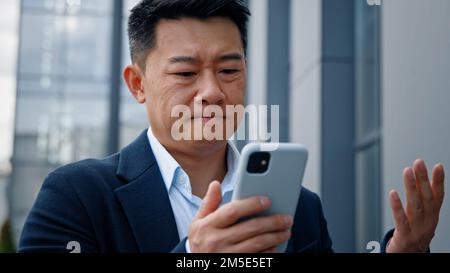 Triste asiatico medio-vecchio uomo adulto pazzo infelice uomo d'affari sensazione infastidito con l'uso di smartphone rotto problema di batteria scarica arrabbiato avere problema con Foto Stock
