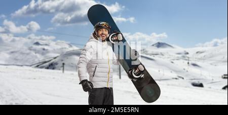 Felice giovane uomo che tiene uno snowboard e guarda la macchina fotografica su una montagna Foto Stock