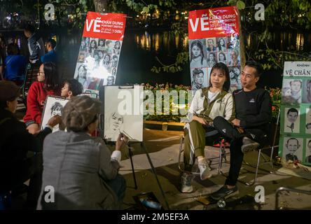 Una giovane coppia si siede per avere il loro ritratto disegnato vicino al lago Hoan Kiem nel centro di Hanoi, Vietnam. Foto Stock