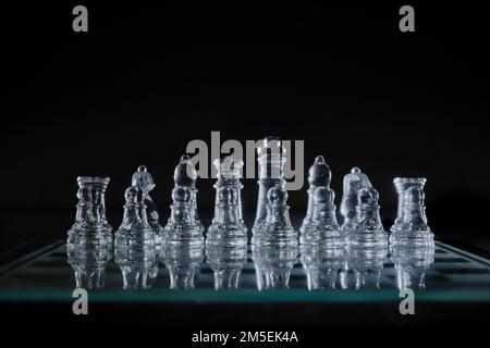Un primo piano di pezzi di scacchi di cristallo su una tavola di vetro su sfondo nero Foto Stock