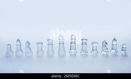 Una fila di pezzi di scacchi in vetro in una fila su uno sfondo bianco con spazio copia Foto Stock