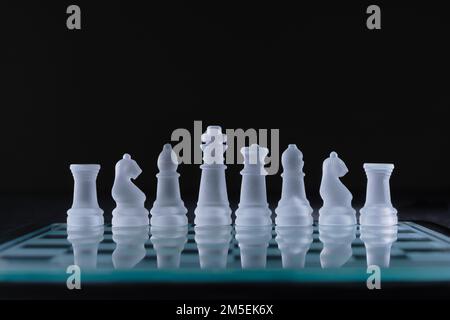 Un primo piano di una fila di pezzi di scacchi di cristallo su una tavola di vetro su sfondo nero Foto Stock