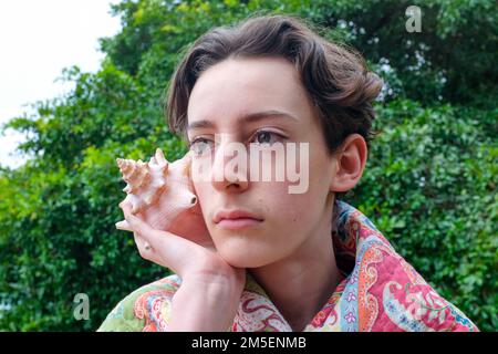 Teen caucasico che tiene una conchiglia gigante Foto Stock