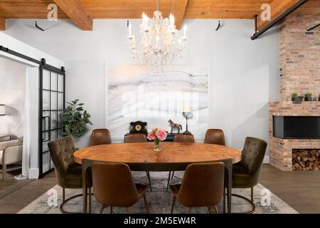 Una sala da pranzo mansardata con soffitto in legno a vista, un lampadario sopra un grande tavolo da pranzo e un caminetto in mattoni. Foto Stock