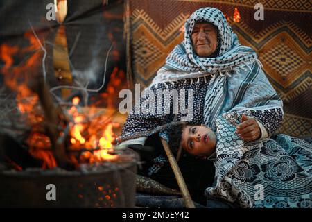 Una madre palestinese riscalda i suoi figli durante il freddo nella zona di Beit Lahia, nella striscia di Gaza settentrionale. Le relazioni delle istituzioni per i diritti umani affermano che oltre il 70 per cento della popolazione di Gaza vive al di sotto della soglia di povertà stabilita dagli standard internazionali. Palestina. Foto Stock