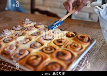 donna che stendono un grande foglio di dolci alla cannella appena sfornati ordinatamente posti in file in attesa di essere glassato con glassa bianca Foto Stock