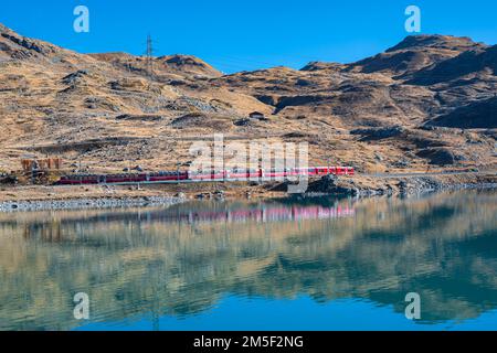 Splendida vista panoramica sul treno rosso “Bernina Express“ che passa sul lago “Lago Bianco” vicino al Passo Bernina nelle Alpi Svizzere. Foto Stock