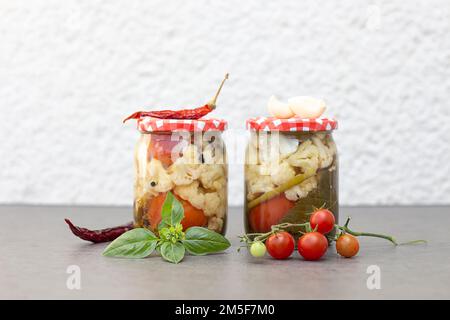 Vasetti di vetro con pomodori sottaceto. Cibo vegetariano conservato. Vasetti con verdure varie sottaceto. Foto Stock
