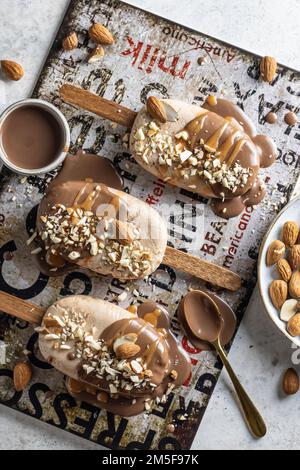 Alcune deliziose gelaterie vegane fatte in casa o popsicle ricoperte di cioccolato e noci vista dall'alto, piatto. Verticale Foto Stock