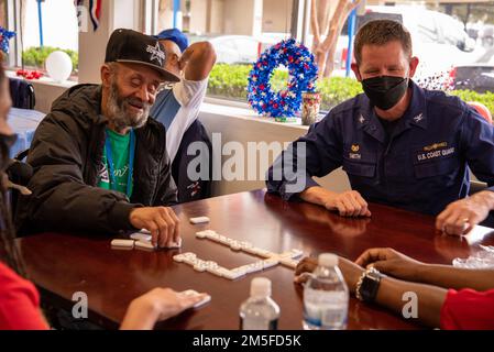 Il capitano Jason Smith, comandante del settore della Guardia Costiera Houston-Galveston, parla e gioca a domino con un veterano durante un evento di volontariato organizzato dalla Campagna Federale presso la casa di un veterano di Houston, Texas, il 11 marzo 2022. I membri hanno cucinato e tagliato il pranzo ai residenti locali accanto agli Stati Uniti L'immigrazione e l'applicazione delle dogane e il Michael E. DeBakey Veterans Affairs Medical Center, come parte di un evento volontario in collaborazione con gli Stati Uniti Vets Houston e la Veteran Initiative. Foto Stock