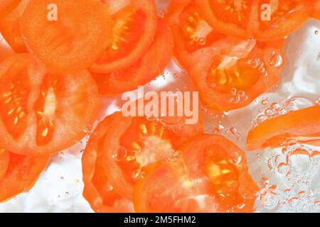 Primo piano di pomodoro in liquido con bolle. Fette di pomodoro rosso maturo in acqua. Primo piano fette fresche di pomodoro rosso su sfondo bianco Foto Stock