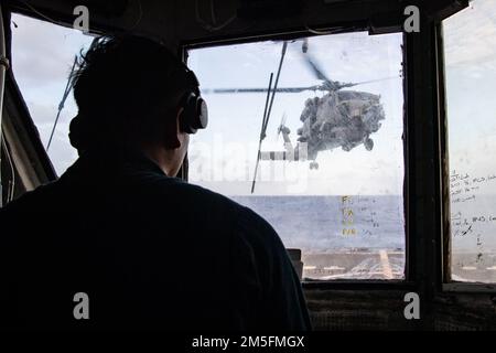 MAR DELLE FILIPPINE (14 marzo 2022) Lt. j.g. Jian Miclat, di Chula Vista, California, funge da ufficiale di controllo dell'elicottero e coordina con il cartello di atterraggio e ponte per il lancio di un elicottero MH-60R assegnato a Helicopter Maritime Strike Squadron (HSM) 51 dal ponte del cacciatorpediniere missile guidato classe Arleigh Burke USS Dewey (DDG 105) Mentre si svolgono operazioni di routine in corso nell'area di responsabilità della flotta USA 7th. Dewey è assegnato a Destroyer Squadron (DESRON) 15 ed è in corso il supporto di un indoPacifico libero e aperto. CTF 71/DESRON 15 è il lar della Marina Foto Stock
