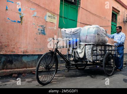 Un uomo bengalese che trasporta grandi pacchi su un risciò in bicicletta a Kolkata, India. Foto Stock