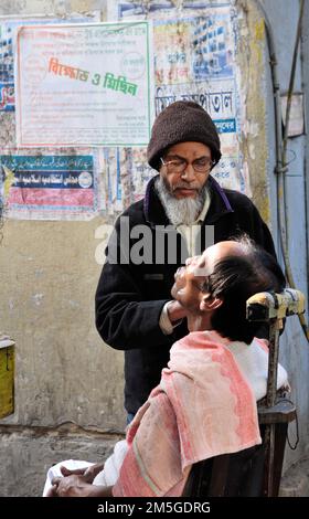 Un barbiere rasa un uomo a Kolkata , India. Foto Stock