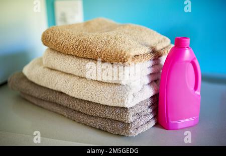 Picciolisci e spazza. una bottiglia di detergente accanto a una pila di asciugamani piegati. Foto Stock