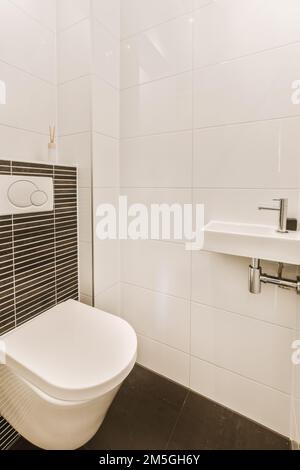 un bagno moderno con piastrelle bianche e nere alle pareti, toilet e lavandino in camera è pulito e pronto all'uso Foto Stock