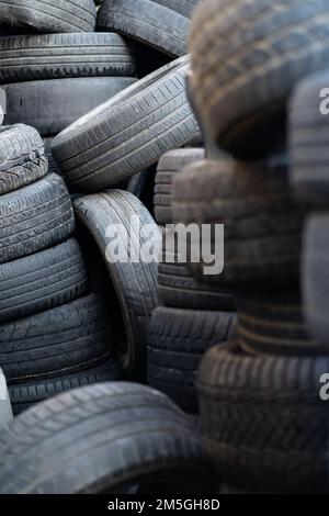 Vecchi pneumatici di gomma usati impilati con pali alti. Rifiuti pericolosi che richiedono il riciclaggio e lo smaltimento. Foto Stock